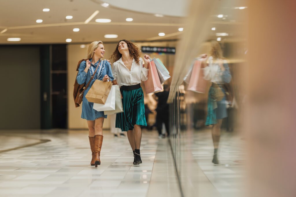Shot of two attractive girlfriends smiling while walking with shopping bags in the city mall during the day.